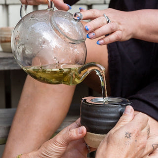Pouring herbal tea from a glass teapot into a ceramic cup