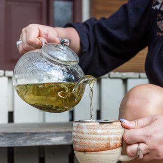 Pouring herbal tea from a glass teapot into a ceramic cup