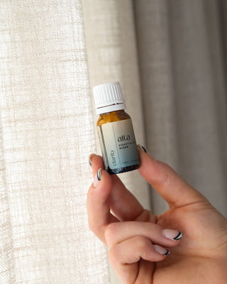 A hand holding the Clarity essential oil blend bottle by a window