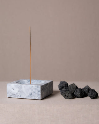 Marble incense holder with an incense stick standing upright and lava stones beside it